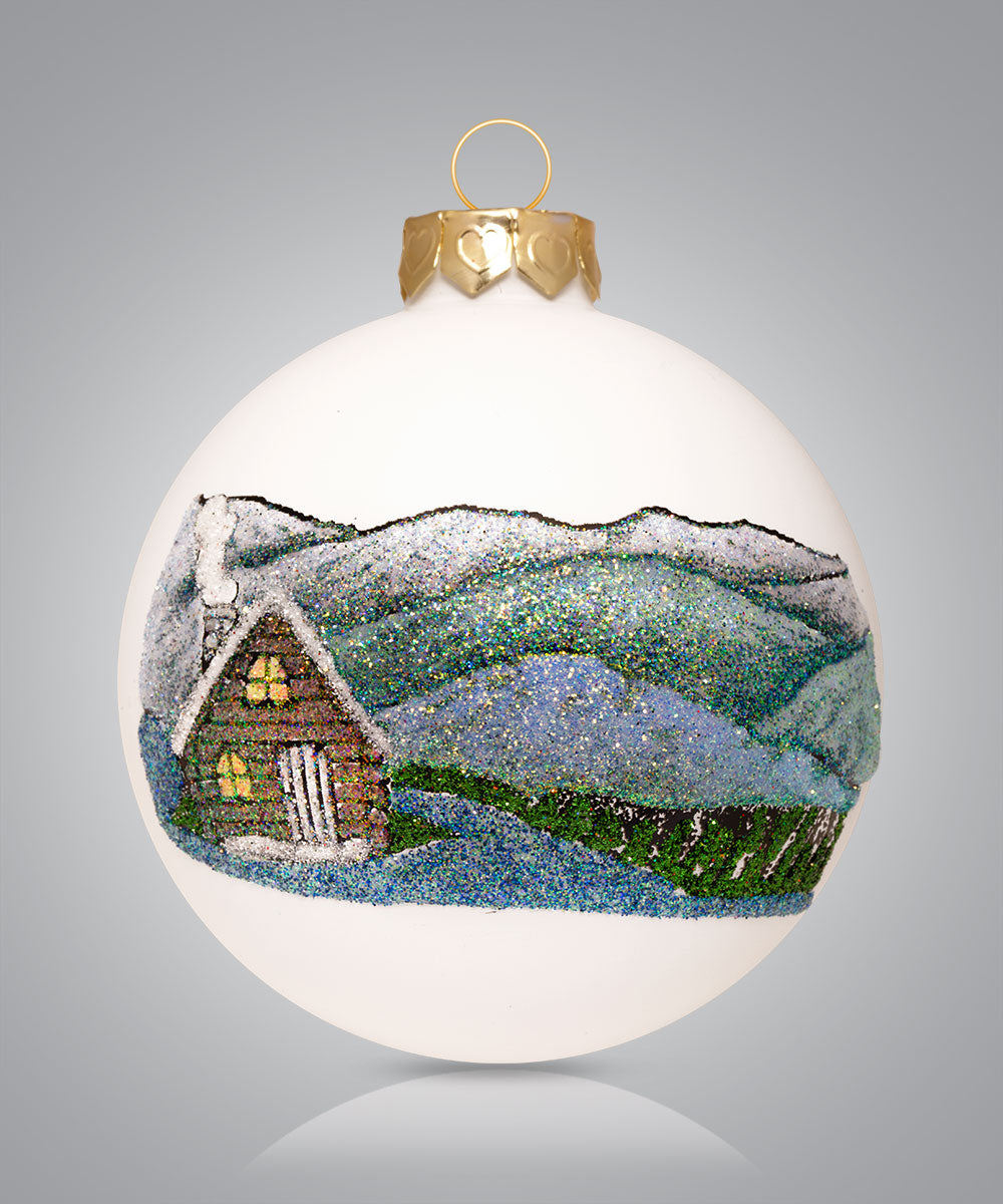 Hand-painted glass ornament depicting a cabin with blue mountains